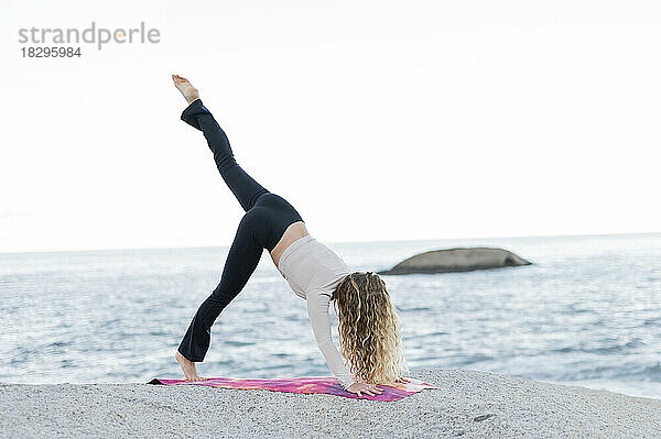 Frau praktiziert Yoga vor dem Meer