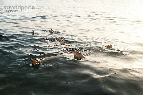 Frau schwimmt bei Sonnenuntergang auf dem Meer