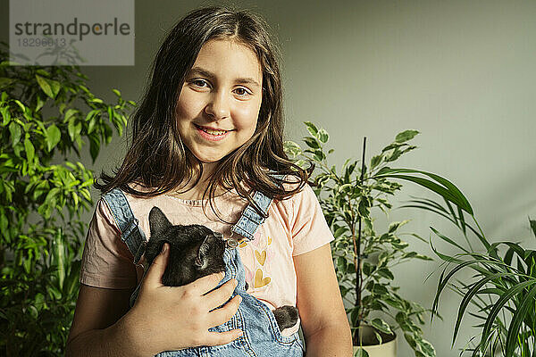 Smiling girl with cat in front of plants at home