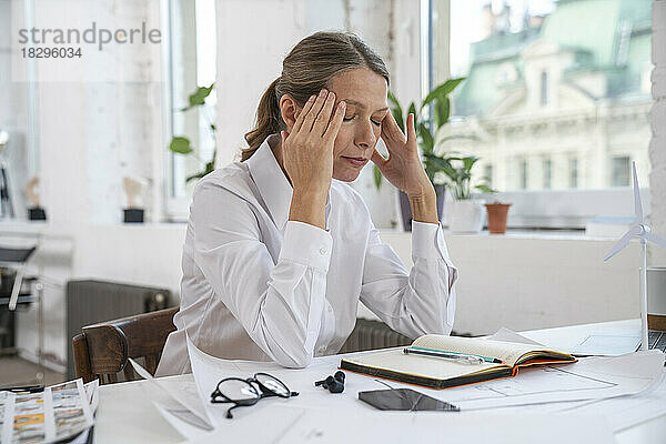 Frustrierte Geschäftsfrau mit Kopf in den Händen sitzt im Büro