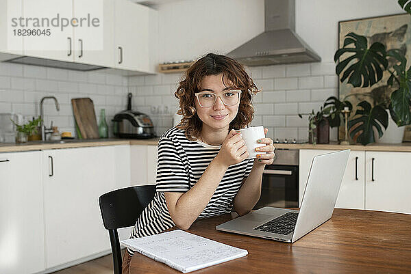 Freelancer with cup of coffee sitting with laptop at table