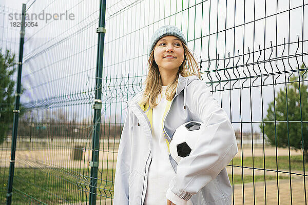 Nachdenkliches Mädchen mit Strickmütze steht mit Fußball