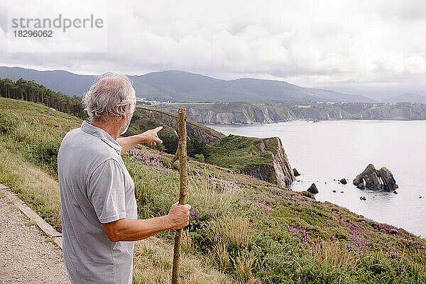 Älterer Mann mit Stock  der auf Berge zeigt
