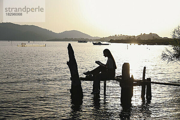 Silhouette einer jungen Frau  die auf einer handgefertigten Angelplattform im Meer sitzt