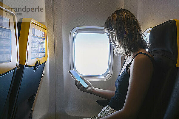 Frau benutzt Smartphone im Flugzeug