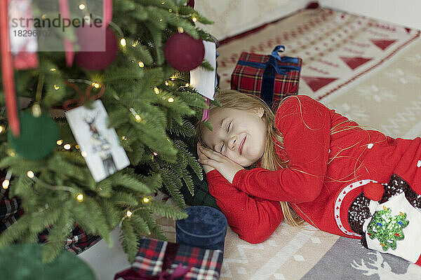 Lächelndes Mädchen entspannt sich zu Hause am Weihnachtsbaum auf dem Teppich