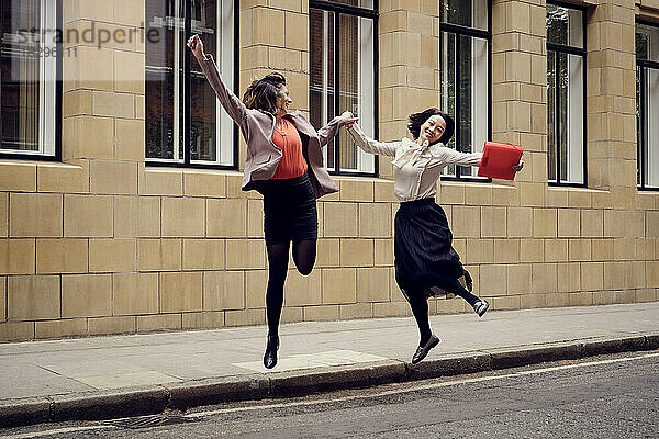 Fröhliche Geschäftsfrau springt mit Kollege auf der Straße