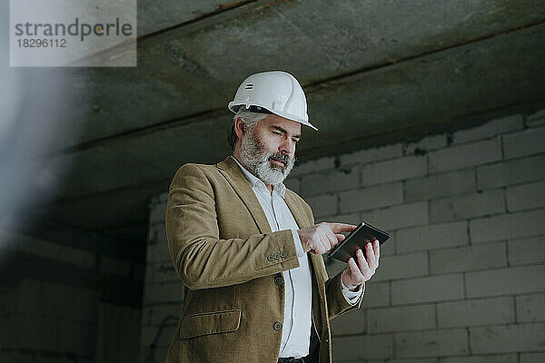 Architekt mit Schutzhelm und Tablet-PC steht auf der Baustelle