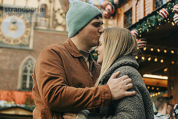 Mann küsst Frau auf dem Weihnachtsmarkt auf die Stirn