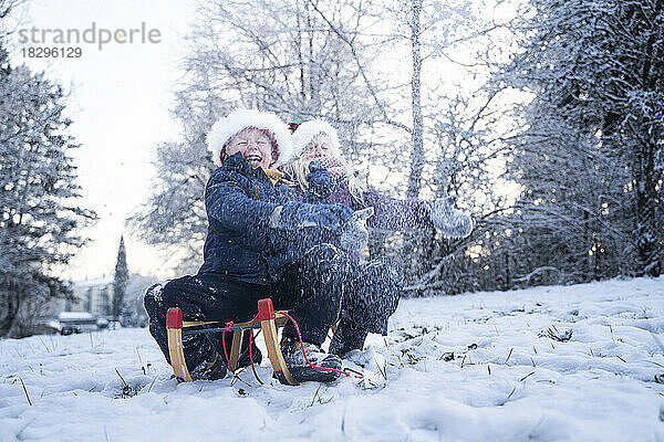 Fröhliche Jungen und Mädchen mit Weihnachtsmützen spielen im Schnee