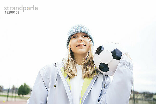 Mädchen steht mit Fußball unter klarem Himmel