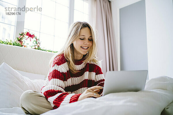 Glückliches Mädchen  das zu Hause einen Laptop im Bett benutzt