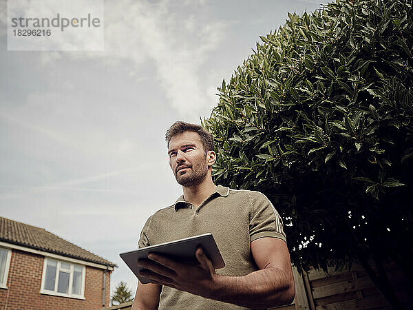Mann steht mit digitalem Tablet im Garten