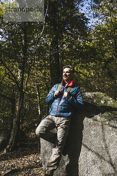 Reifer Mann lehnt an einem sonnigen Tag auf einem Felsen im Wald