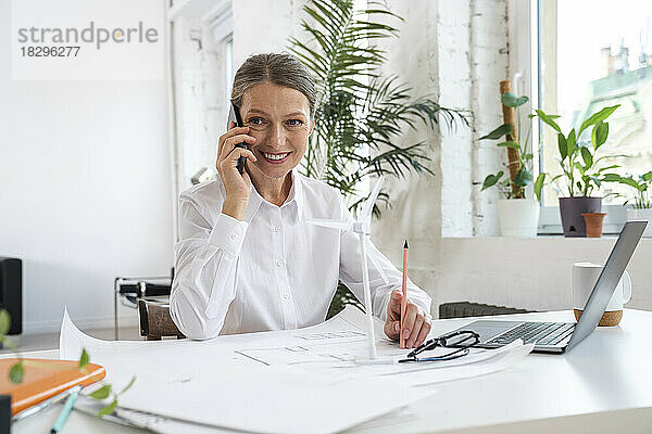 Lächelnde reife Geschäftsfrau  die im Büro über ihr Smartphone spricht