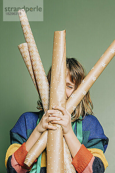 Girl with wrapping paper rolls standing in front of green wall