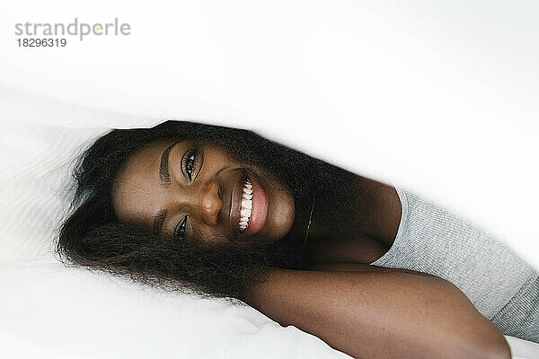 Happy young woman under white blanket on bed