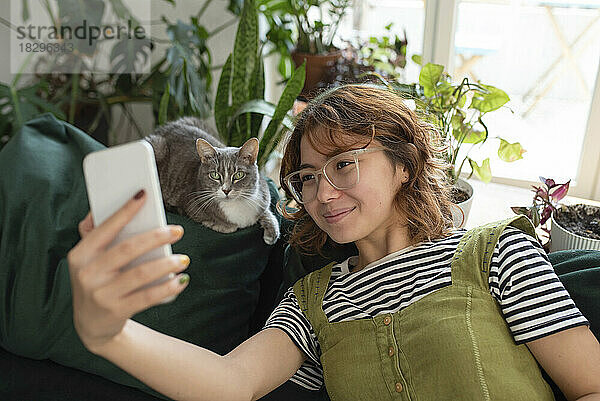 Lächelnde Frau macht ein Selfie mit Katze auf der heimischen Couch