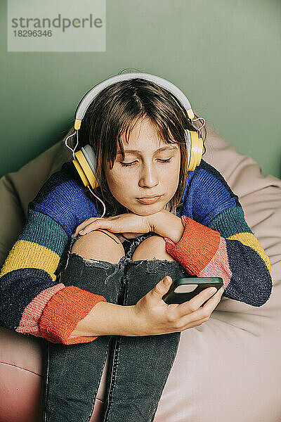 Mädchen trägt Kopfhörer und nutzt Smartphone zu Hause