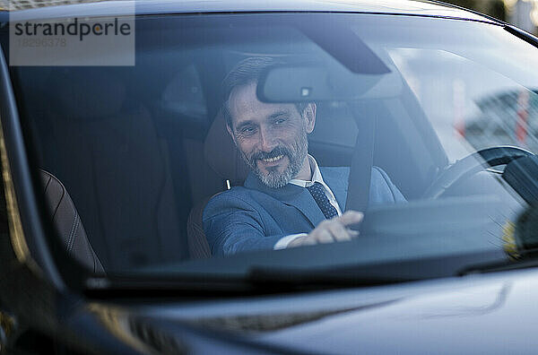 Lächelnder reifer Geschäftsmann überprüft GPS  gesehen durch die Windschutzscheibe des Autos