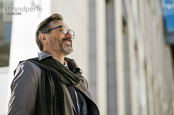 Lächelnder reifer Geschäftsmann mit Brille vor Bürogebäude