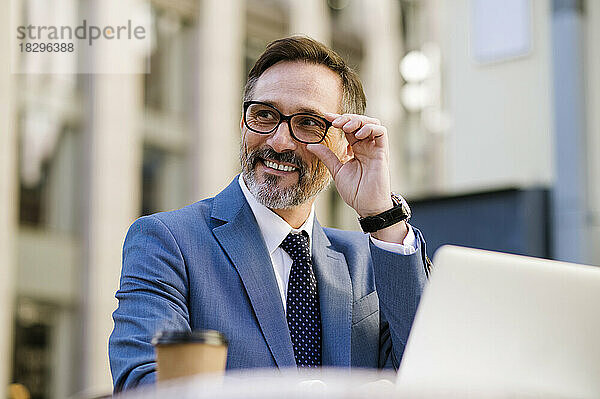 Smiling mature businessman adjusting eyeglasses sitting in cafe