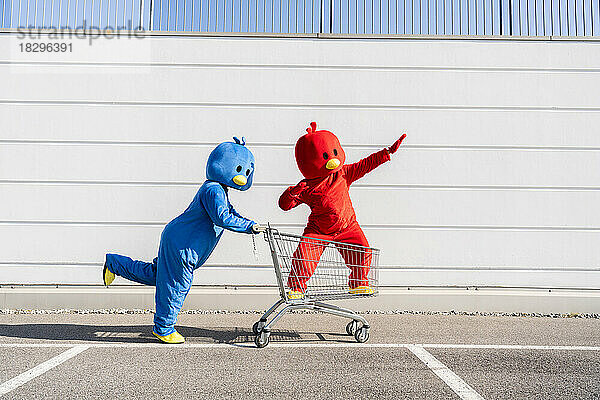 Freunde in blauen und roten Kostümen amüsieren sich mit einem Einkaufswagen an der Wand