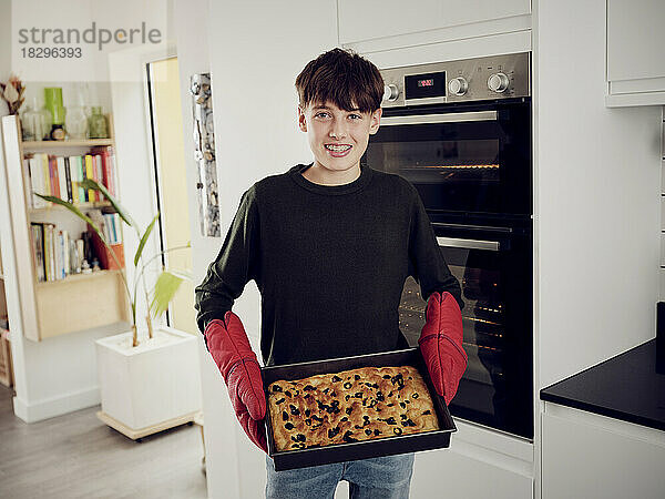 Portrait of boy holding baking tray with fresh focaccia bread in the kitchen