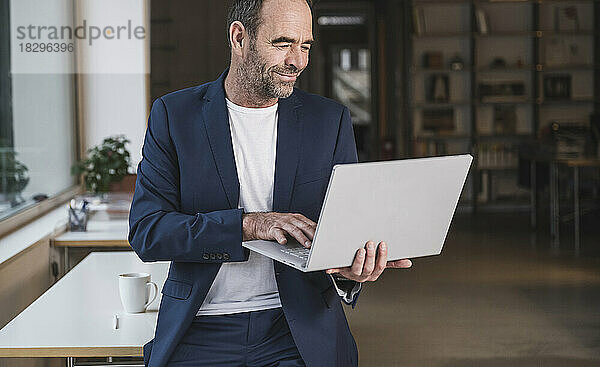 Lächelnder reifer Geschäftsmann  der im Büro am Laptop arbeitet