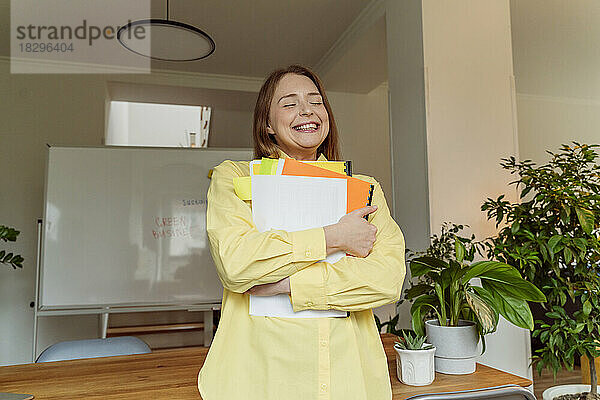 Happy businesswoman with documents standing by desk in office