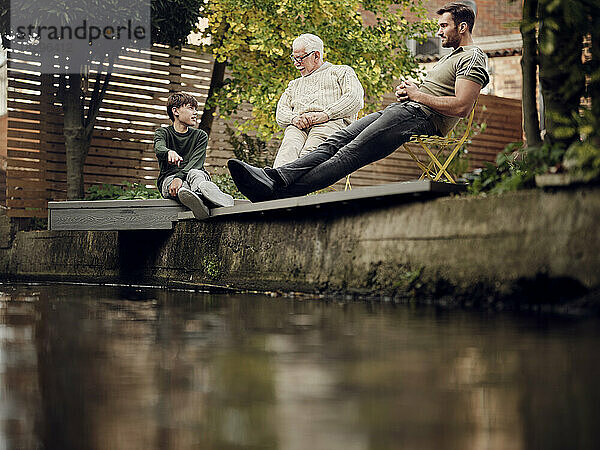 Vater  Sohn und Enkel sitzen am Gartenteich und unterhalten sich und entspannen sich
