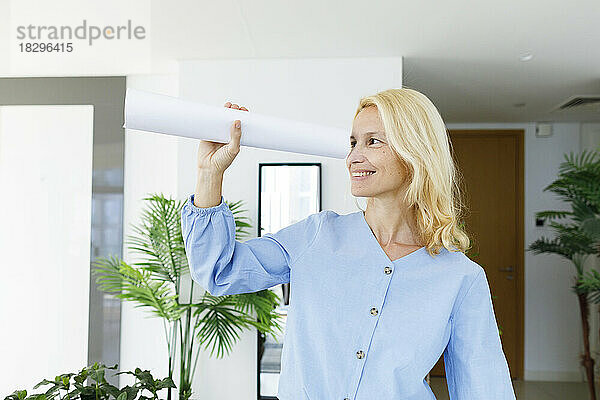 Happy young woman looking through rolled paper at home