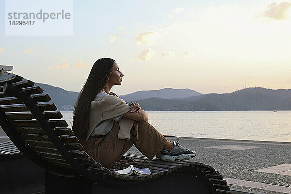 Nachdenkliche Frau sitzt bei Sonnenuntergang auf einem Liegestuhl
