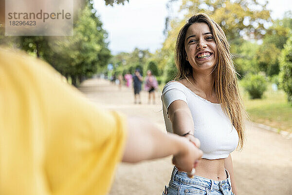 Happy woman holding friends hand in park