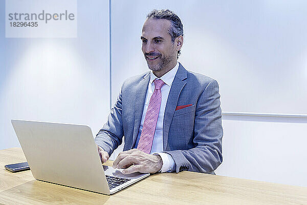 Lächelnder Geschäftsmann  der im Büro am Laptop arbeitet