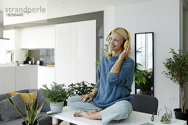 Happy woman wearing wireless headphones listening to music at home