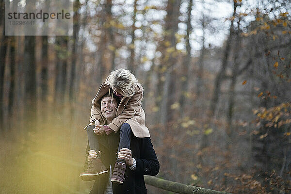 Glücklicher Vater trägt Tochter auf Schultern im Wald