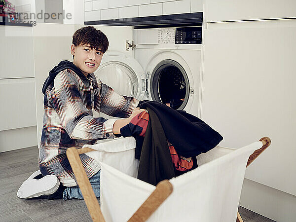 Smiling boy putting laundry into washing machine at home