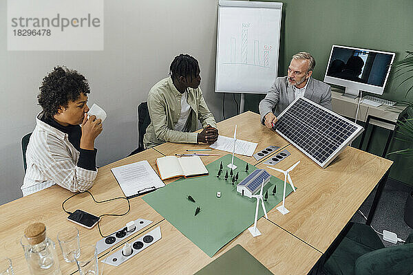 Reifer Geschäftsmann diskutiert mit Kollegen über Solarpanel am Tisch im Büro