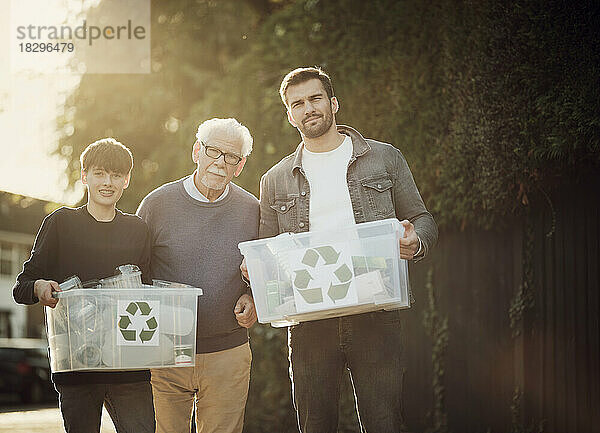Großvater  Vater und Sohn stehen draußen und tragen Recyclingboxen mit getrenntem Müll