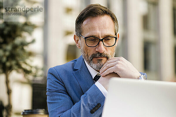 Mature businessman watching laptop sitting at cafe