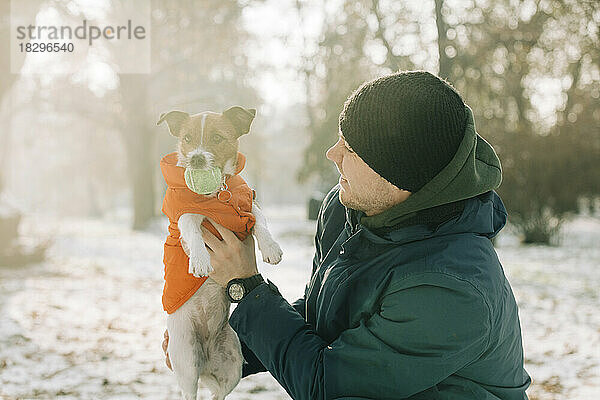 Lächelnder Mann  der im Winter mit seinem Hund spielt