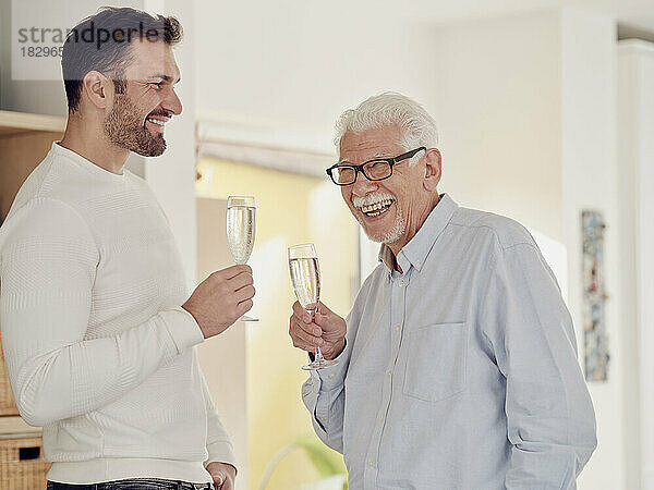 Älterer Mann und erwachsener Sohn feiern zu Hause und stoßen mit Champagner an