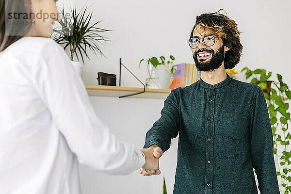 Happy businessman shaking hand with businesswoman in office