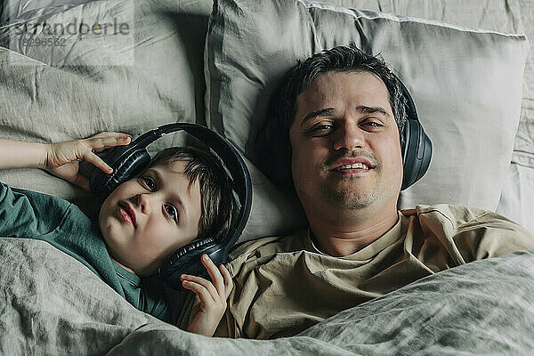 Vater und Sohn tragen Kopfhörer und hören Musik im Bett