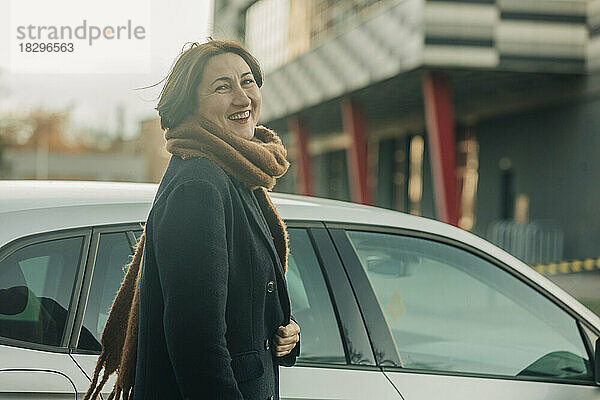 Lächelnde reife Frau mit Schal steht am Auto