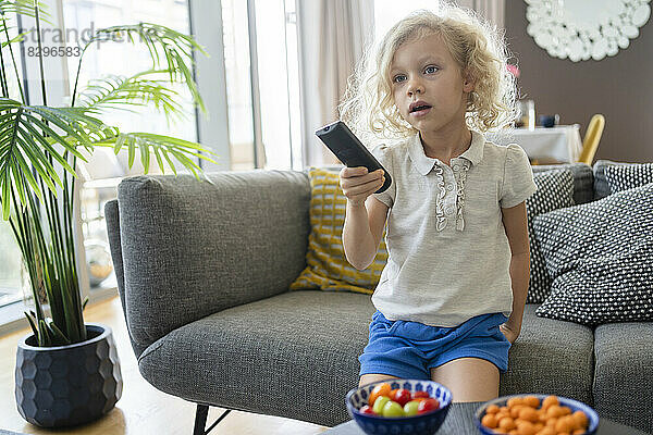 Blond girl holding remote control on sofa at home