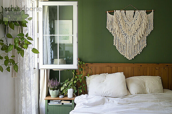 Makramee-Dekoration hängt an der grünen Wand über dem Bett im Schlafzimmer