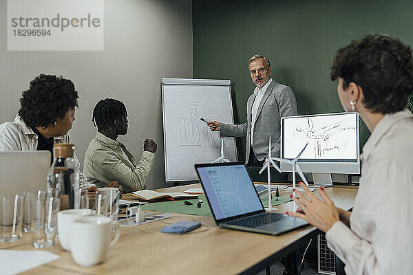 Mature businessman explaining on flipchart to colleagues in office