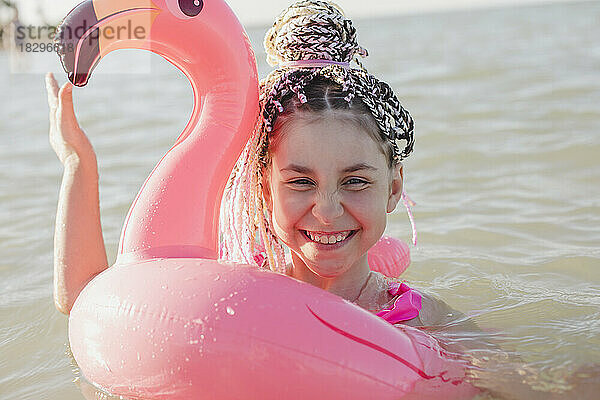 Fröhliches Mädchen mit geflochtenen Haaren  das sich im aufblasbaren Ring mit rosa Flamingos vergnügt